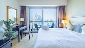 A hotel room with a bed, a desk, a chair, a potted plant, and a view of a cityscape through large windows. - SuperHost - Deluxe Studio with Stunning Marina Views - JW Marriott Dubai Marina (Dubai)