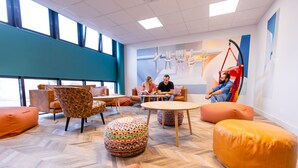 Een moderne zithoek met comfortabele stoelen, een ronde tafel en een kleurrijk kunstwerk aan de muur.