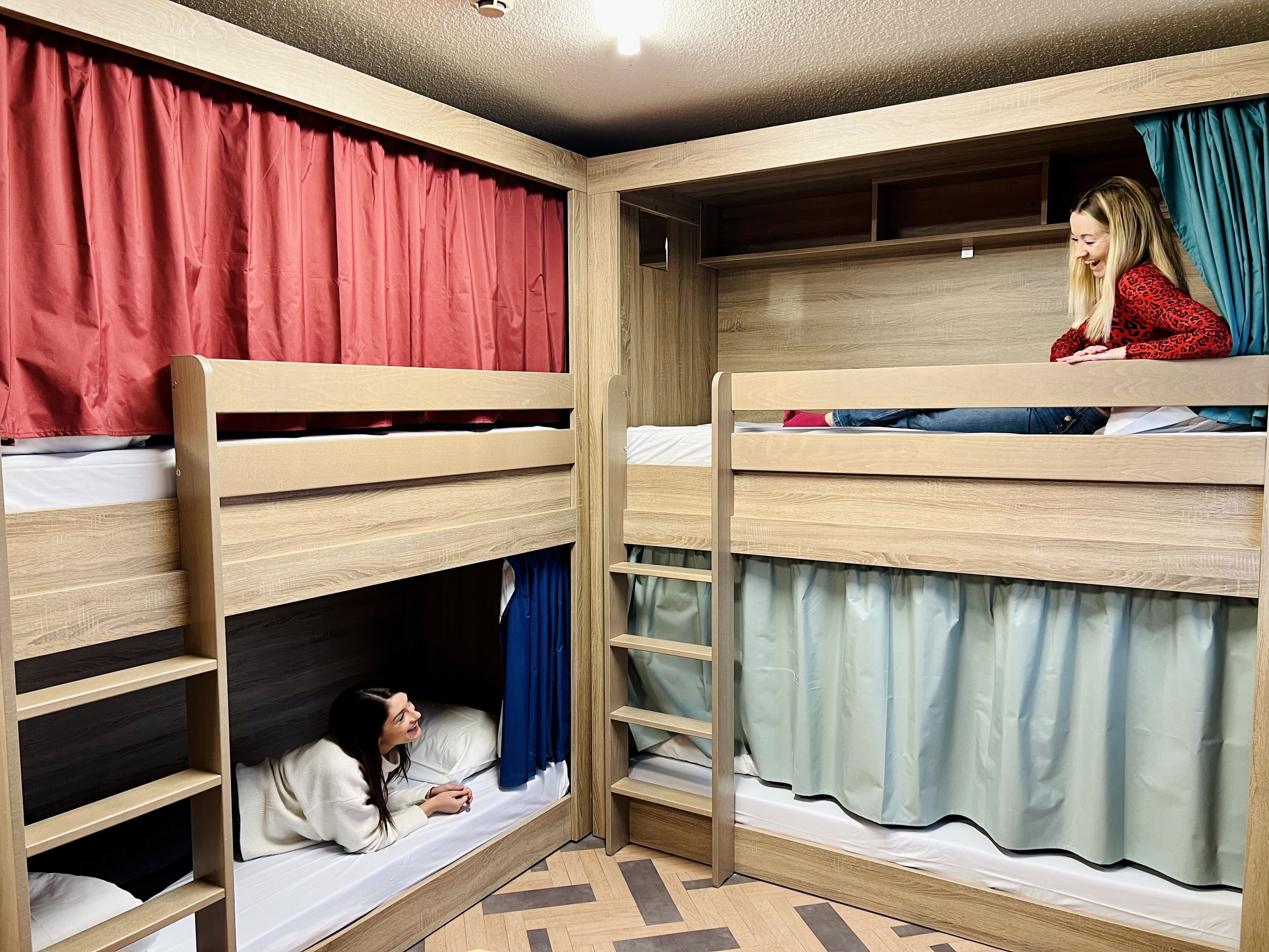 Quarto com beliches de madeira, uma pequena estante e cortina em um dos lados.