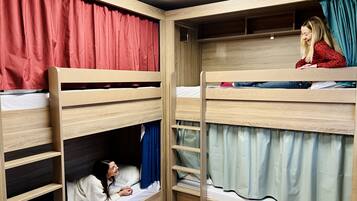 Quarto com beliches de madeira, uma pequena estante e cortina em um dos lados.