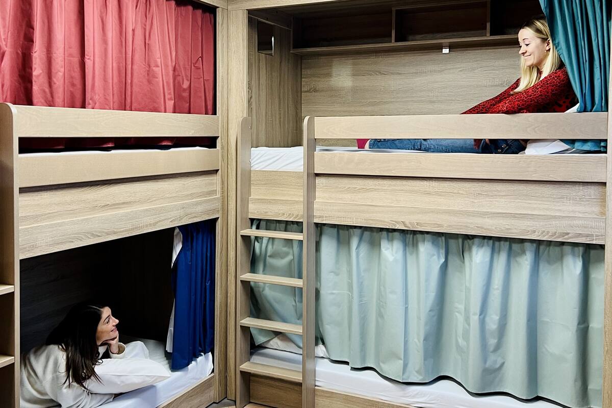 Een slaapkamer met stapelbed, bureau en stoel, een plafondlamp en een raam met gordijnen.