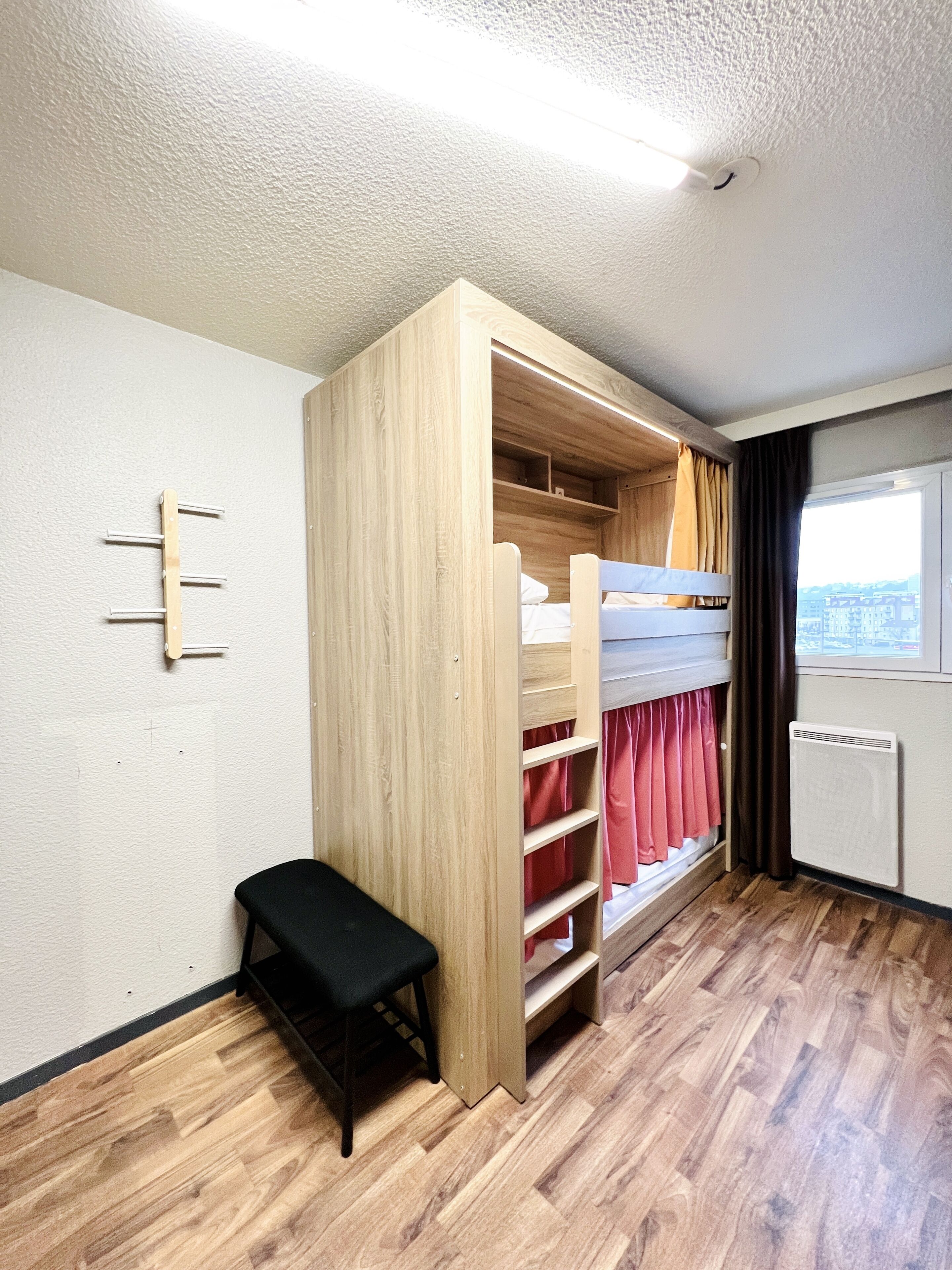 Ein Schlafraum mit Etagenbett, einem Holzschrank, einer kleinen Bank und einem Heizkörper.