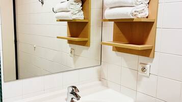 Un bagno con un lavandino bianco, uno specchio e mensole in legno con asciugamani bianchi.