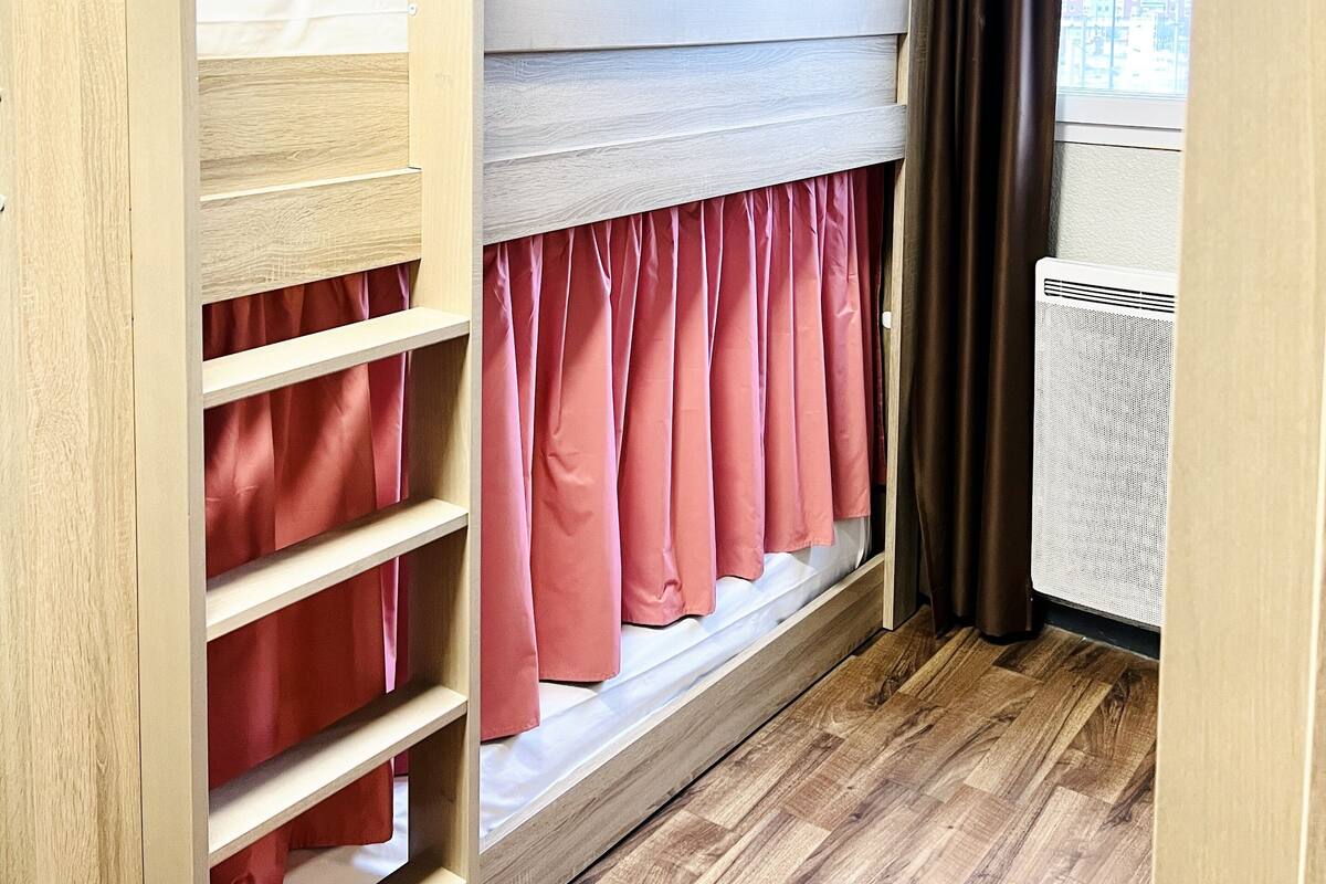 Een slaapkamer met stapelbedden, houten wanden, een raam met gordijnen en een radiator.