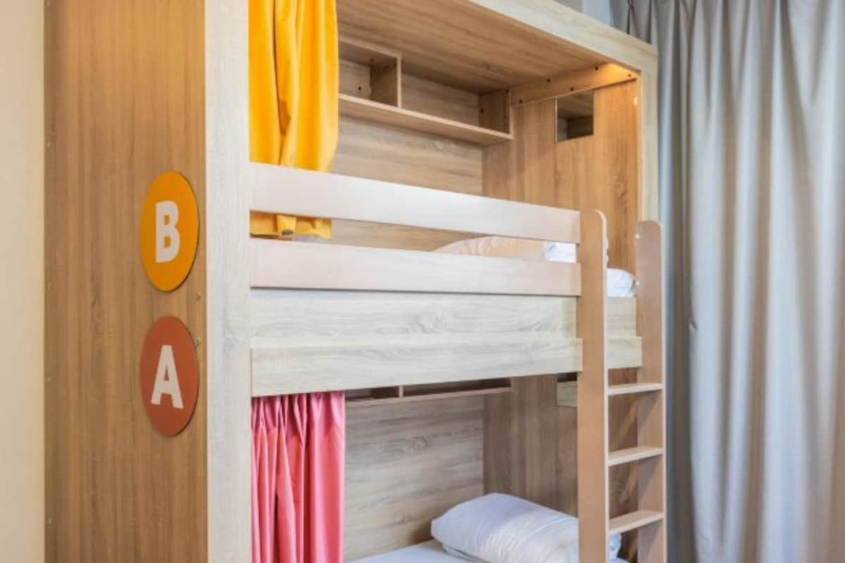 A bunk bed with a wooden headboard and a shelf above it. There are two circular signs with letters 'B' and 'A' on the wall.