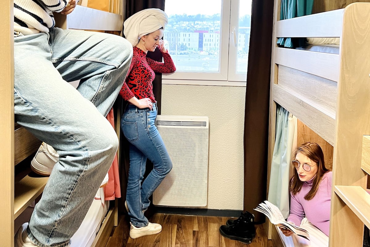 Een kleine kamer met stapelbedden, een raam met gordijnen en een radiator.
