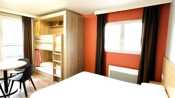 Een hotelkamer met een bed, een bureau en een stoel. Er is een raam met gordijnen.