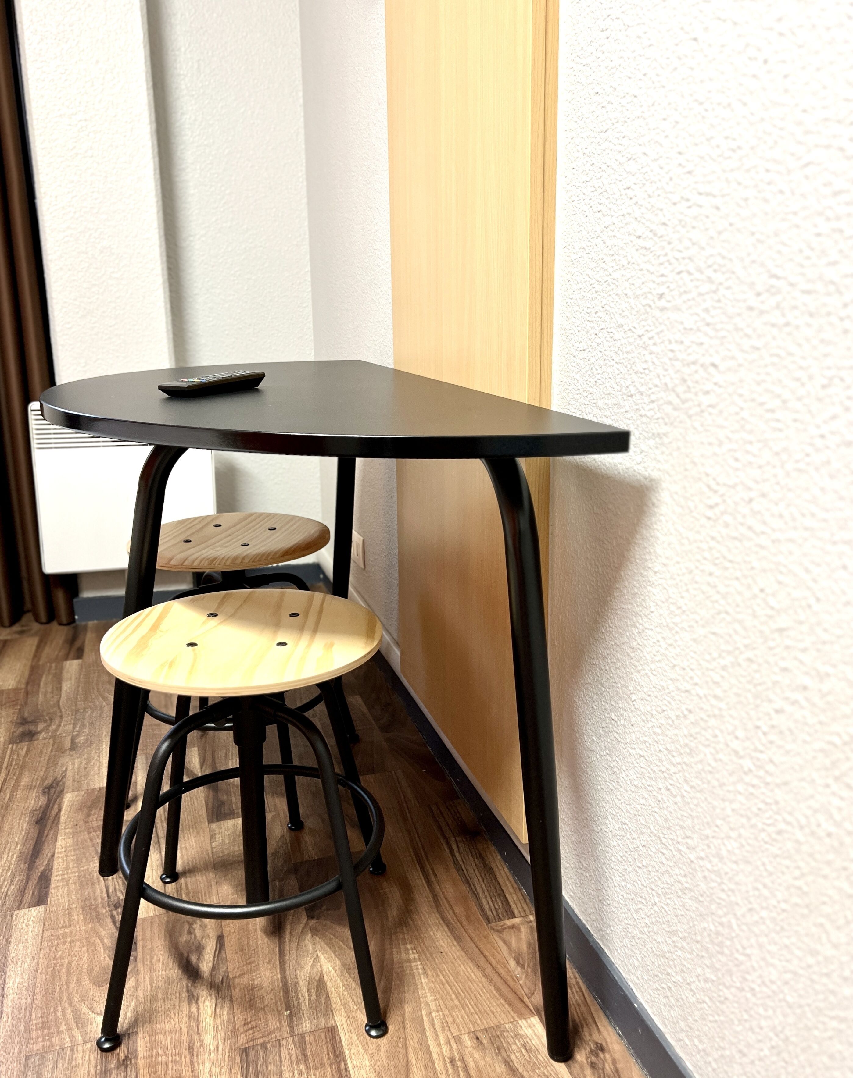 Une petite table ronde noire, sur laquelle se trouve une télécommande, placée à côté d’un tabouret en bois.