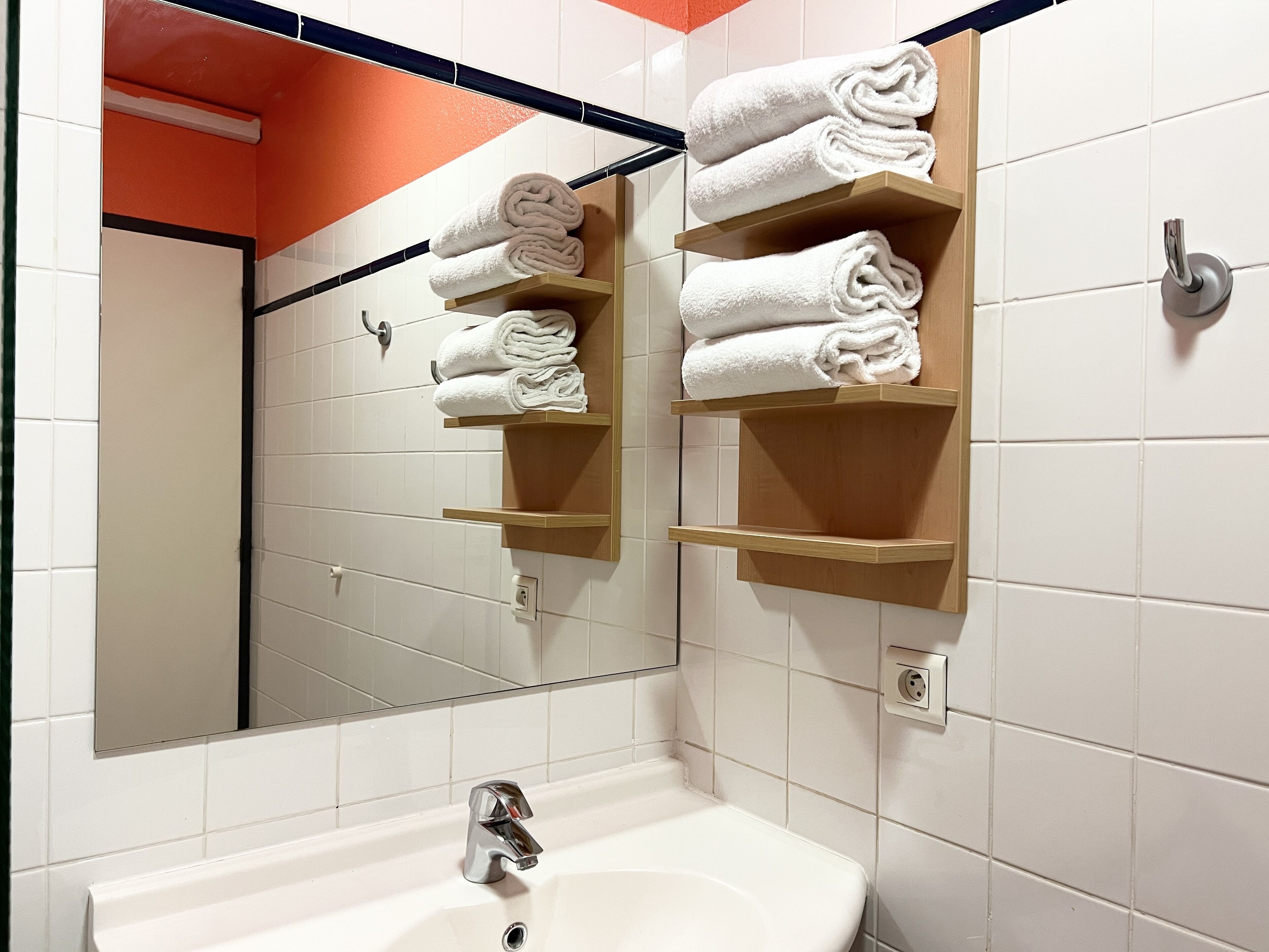 A bathroom with white tiled walls, a white sink, and wooden towel racks holding folded towels.