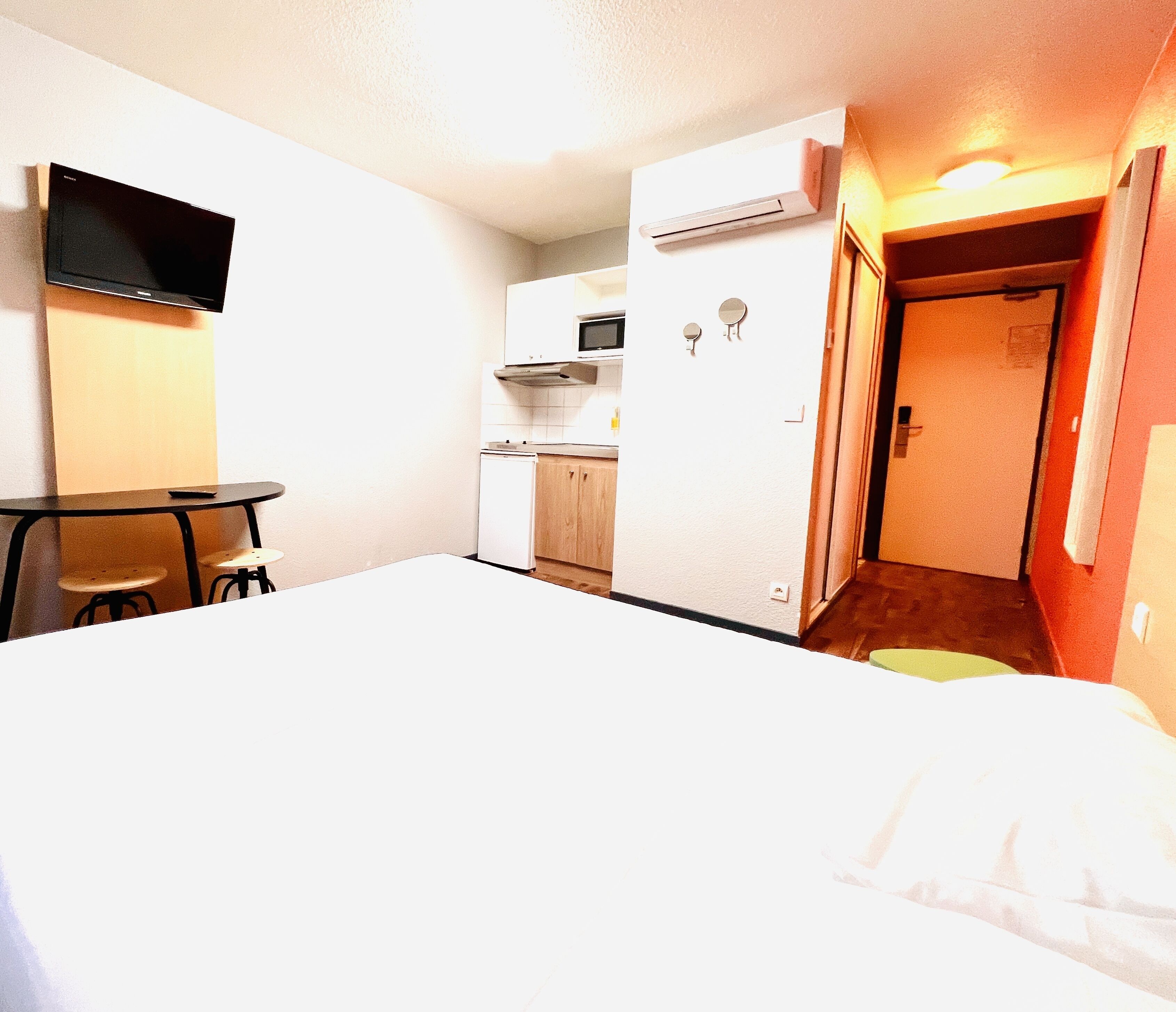 Habitación de hotel con cama, escritorio, silla, microondas y pequeña cocina.