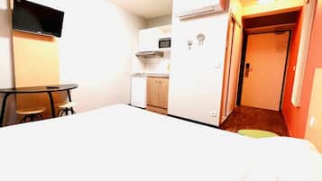 Habitación de hotel con cama, escritorio, silla, microondas y pequeña cocina.