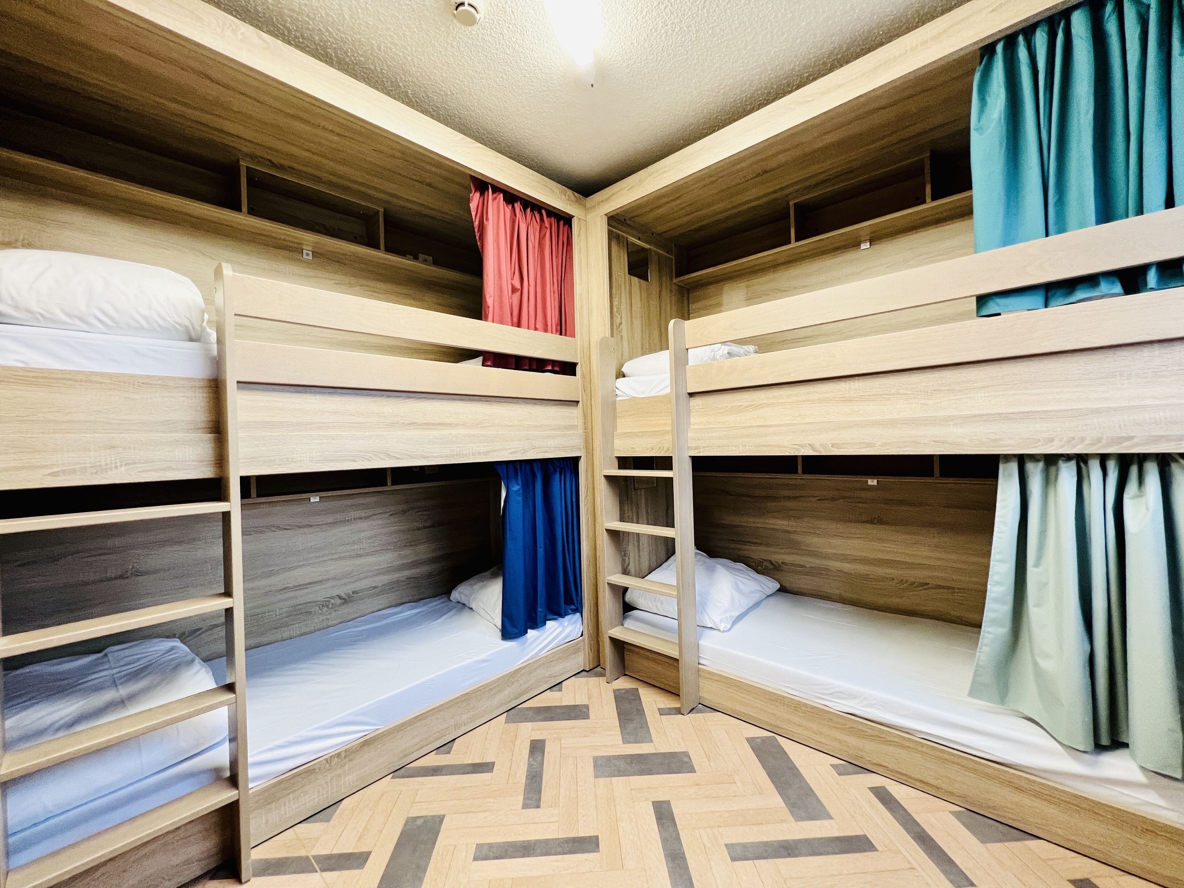 A bunk bed room with wooden bunk beds, a herringbone-patterned floor, and curtains in red, blue, and teal.