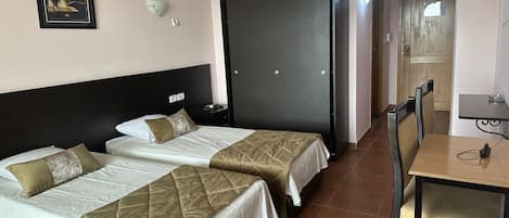 Habitación de hotel con dos camas, un armario, un escritorio con silla y aire acondicionado instalado en la pared.