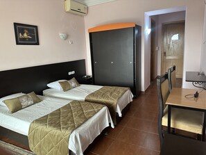 A hotel room with two beds, a wardrobe, a desk with a chair, and a wall-mounted air conditioner. - Hotel Galaxy  (Sfax Ouest)