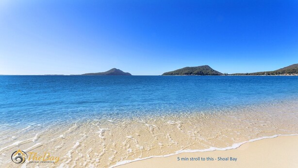 A beach with clear water, sandy shore, and distant hills.