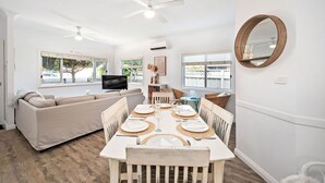 A dining area with a wooden table set for four, a sofa, and a television in the background.