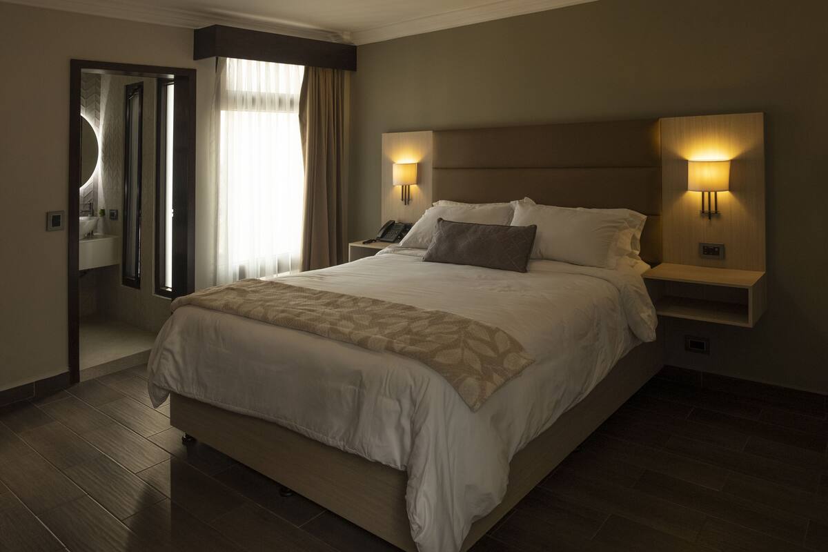A large bed with a headboard, two bedside lamps, a telephone, and a mirror on the wall.
