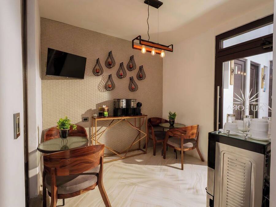 Un espacio habitable compacto con kitchenette, una zona de comedor con sillas de madera, un televisor montado en la pared y una cafetera.