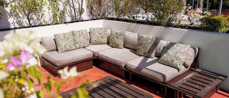 Un sofá modular con cojines estampados, un banco de madera y un patio con baldosas.