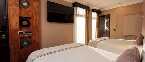 A hotel room with two beds, a TV mounted on the wall, a wooden panel with decorative elements, and a wardrobe.