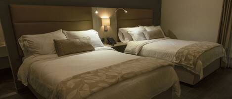 A hotel room with two beds, a nightstand with a phone, and wall-mounted lamps.
