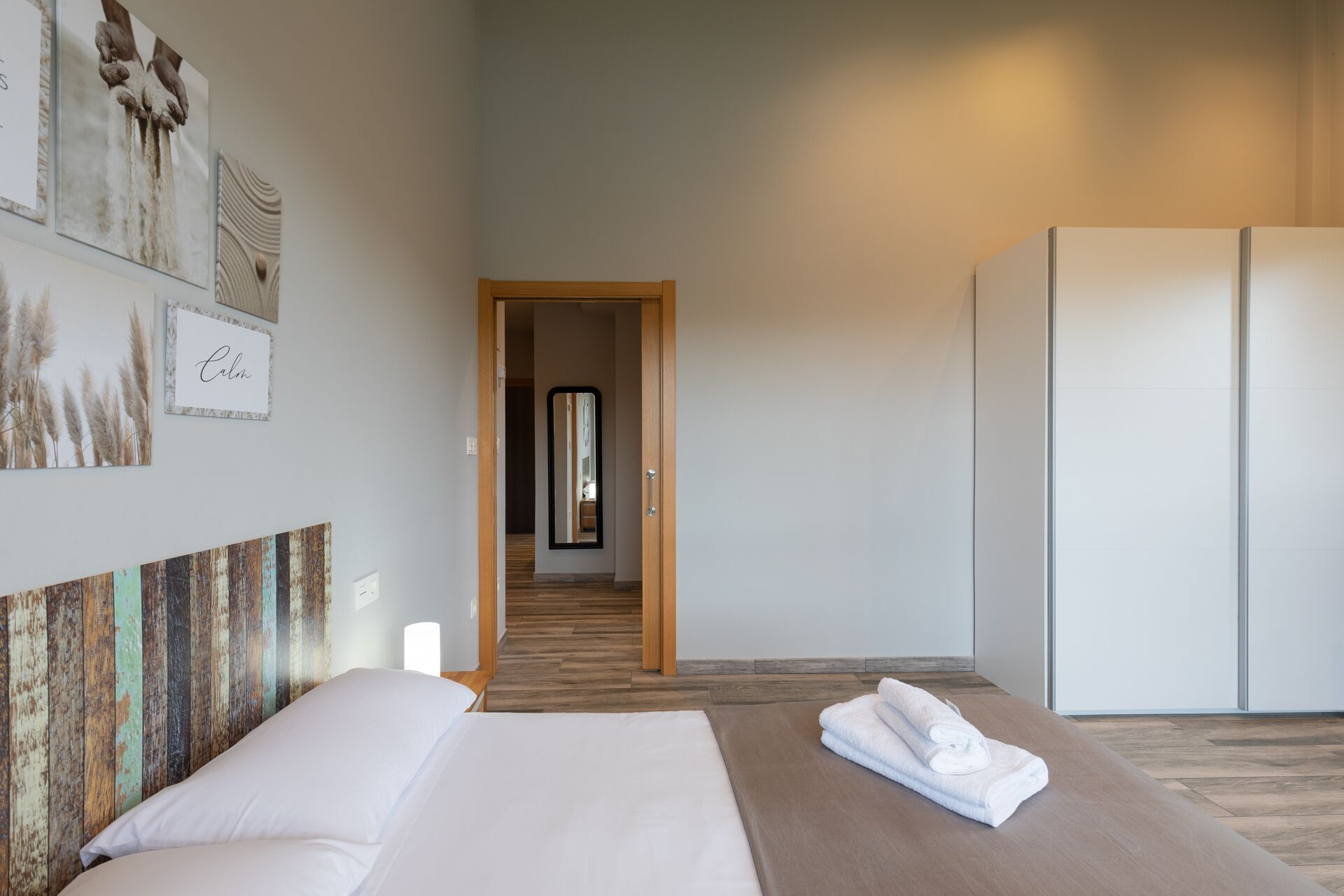 A hotel room with a bed, a wooden floor, a wardrobe, and artwork on the walls.