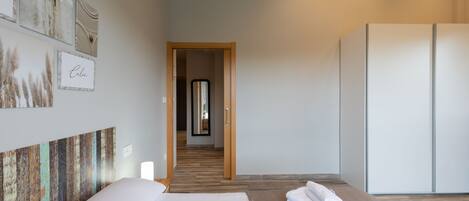 A hotel room with a bed, a wooden floor, a wardrobe, and artwork on the walls.