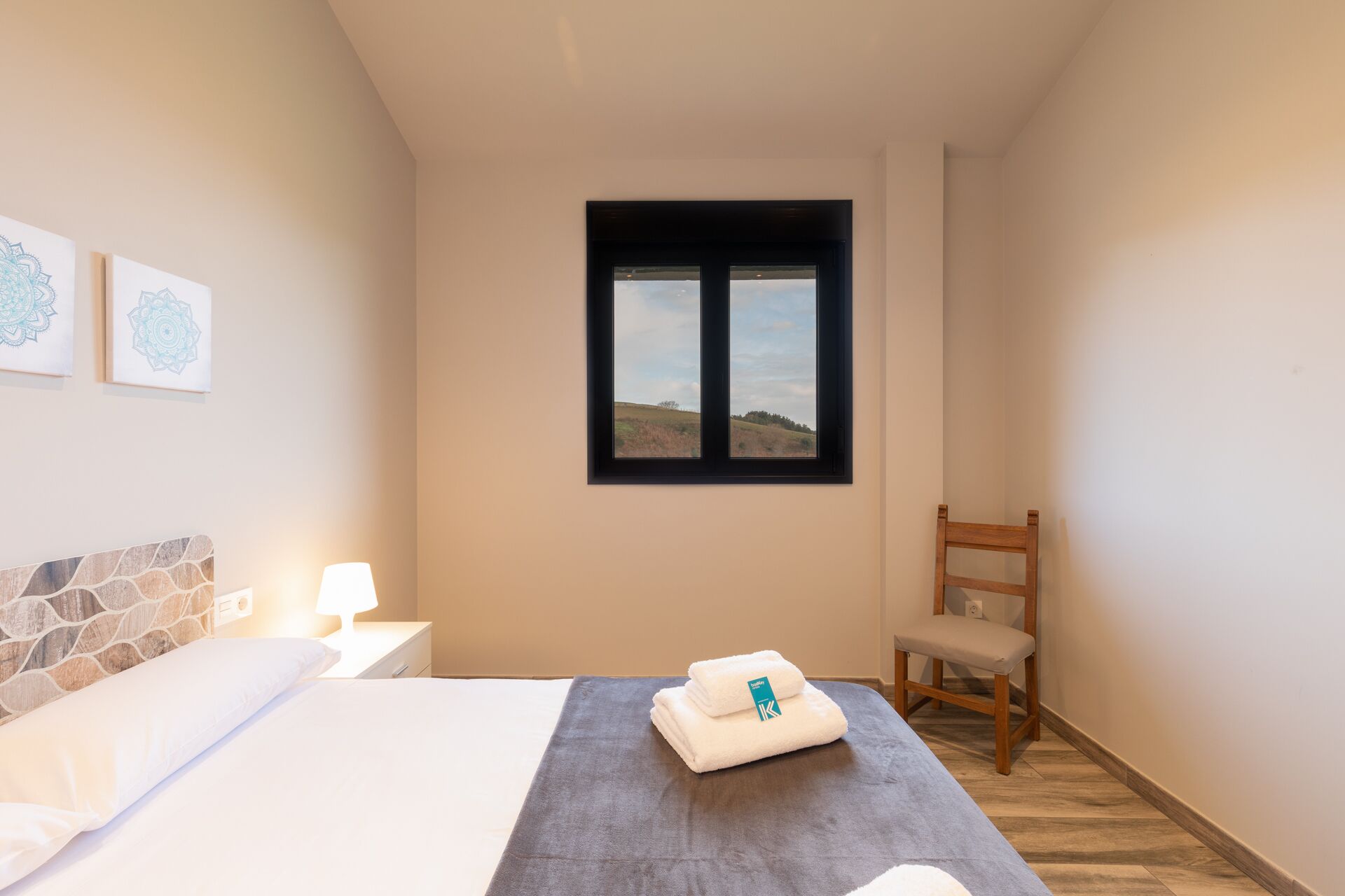 A hotel room with a bed, a window with a view of a landscape, a chair, and a wall with artwork.