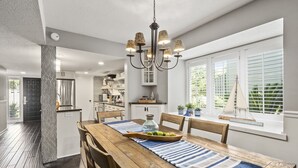 Een moderne keuken met witte kasten, een roestvrijstalen koelkast, en een houten eettafel met een blauw-witte streep geruite placemat.