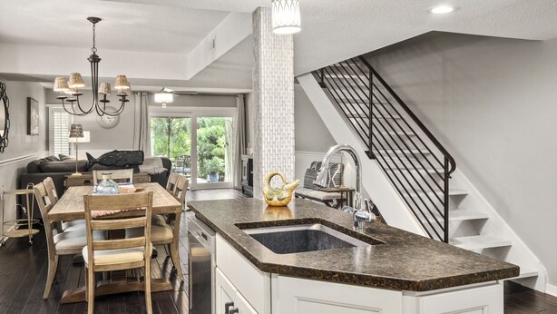 Una cocina amplia con una isla central, un comedor con mesa y sillas de madera, y una escalera que sube a un nivel superior.