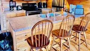 L’intérieur d’une cabane en bois comprend une cuisine, un coin repas et un petit îlot avec des chaises.