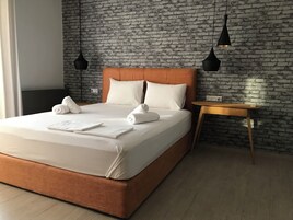 Una habitación de hotel moderna con pared de ladrillo, cabecera de madera y mesita de noche de madera.
