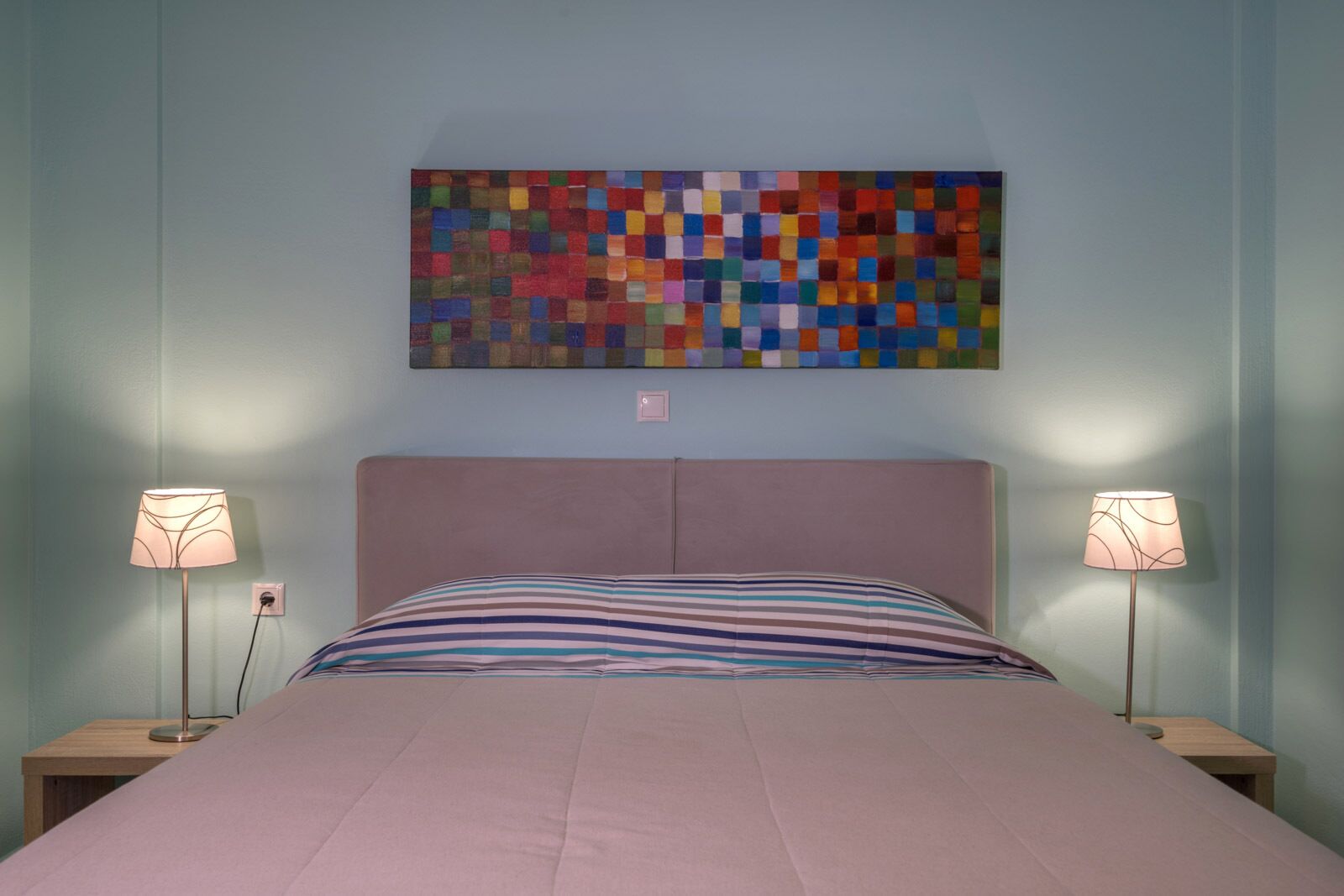 Camera da letto con un letto, due lampade da comodino, un quadro astratto appeso al muro e una presa di corrente.