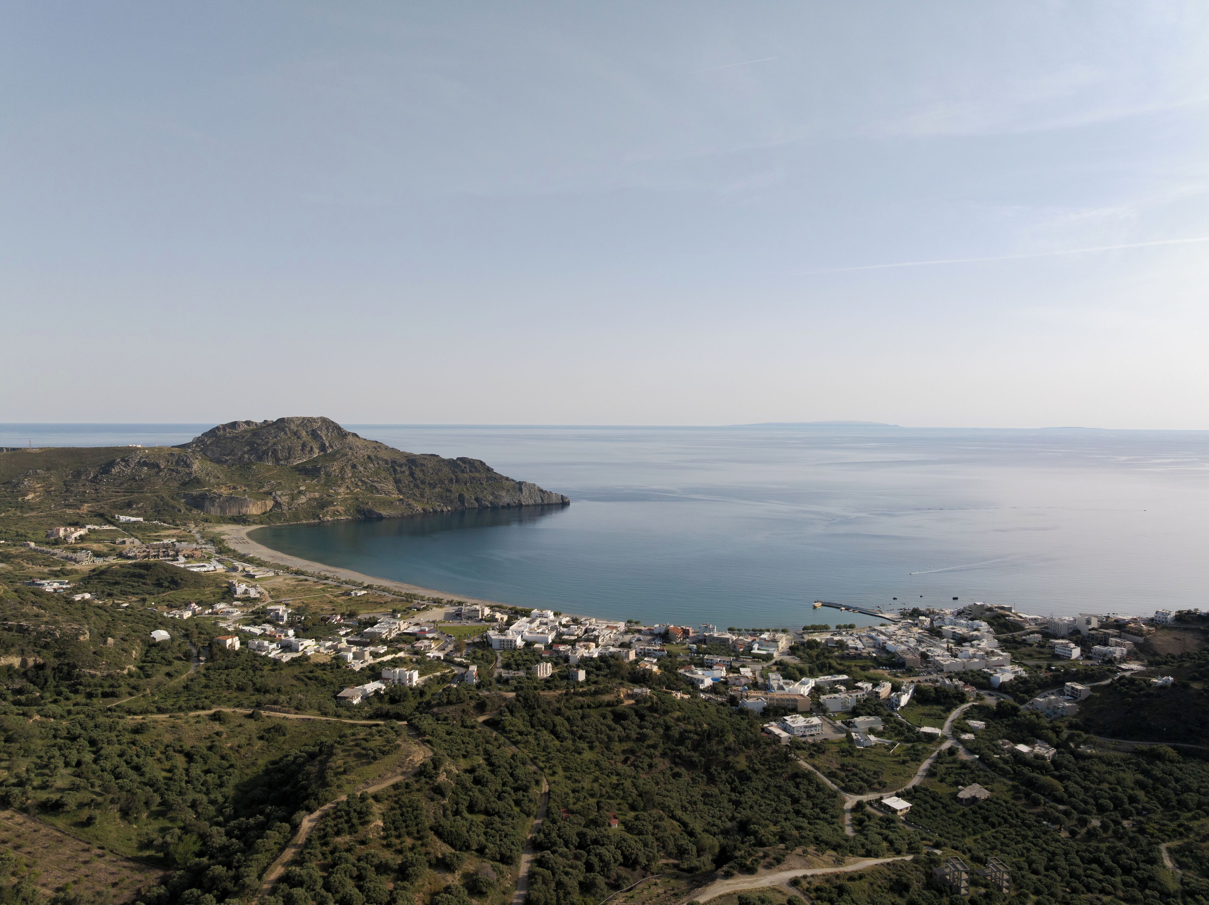 Vista aérea de un pueblo costero con una colina destacada, una playa y un puerto deportivo.