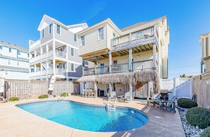 A multi-story building with a pool, outdoor seating, and a thatched-roof structure.