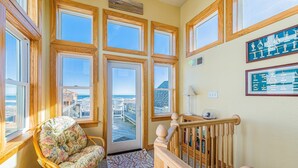 Una habitación con ventanas amplias, una silla de mimbre, una escalera y vista a la playa.
