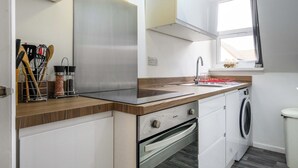 A compact kitchen with a stainless steel range hood, a built-in oven, a washing machine, and a window with curtains. - Sapphire Suite Moseley Birmingham STAE-Homes (Birmingham)
