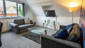 A modern living room with a sofa, a glass coffee table, and a TV mounted on the wall. - Sapphire Suite Moseley Birmingham STAE-Homes (Birmingham)