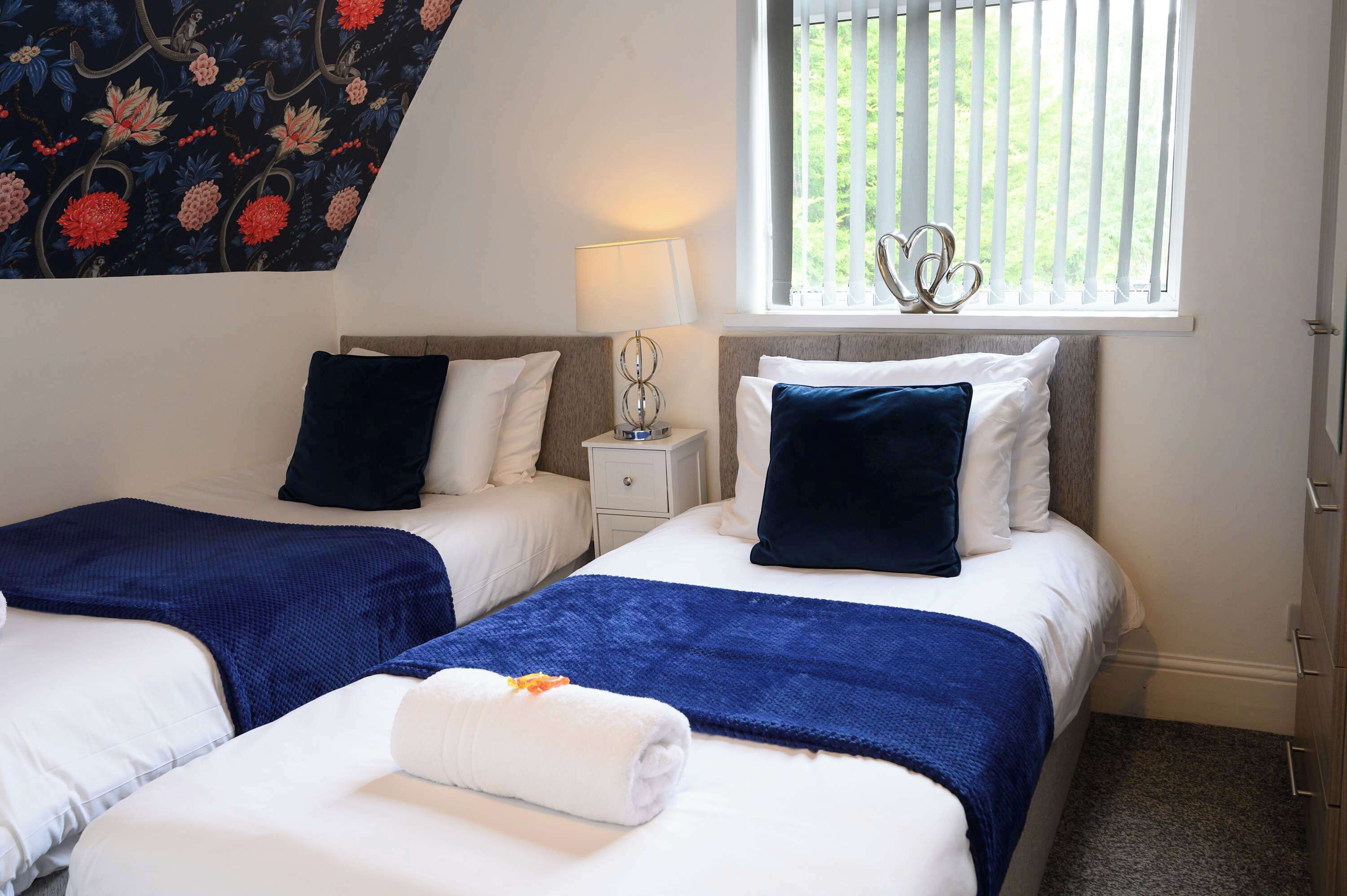 A hotel room with two beds, a window with blinds, a lamp, and a decorative wall piece.
