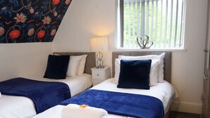 A hotel room with two beds, a window with blinds, a lamp, and a decorative wall piece. - Sapphire Suite Moseley Birmingham STAE-Homes (Birmingham)