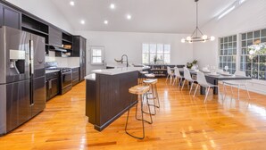 Cozinha moderna com ilha central, banquetas de bar e área de jantar com uma mesa grande e cadeiras.