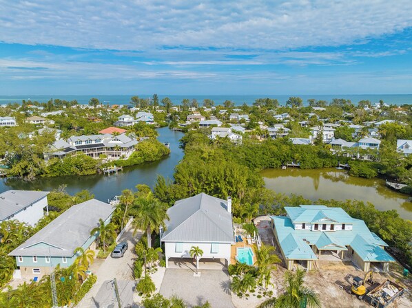 An aerial view of a coastal residential area with houses, a river, and a clear sky. - Sea Jay: Canal front with dock, heated pool, lanai w/outdoor kitchen (Anna Maria)