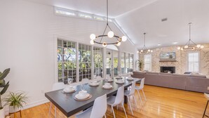 Uma sala de jantar com uma mesa comprida posta para seis pessoas, cadeiras brancas e iluminação pendente.
