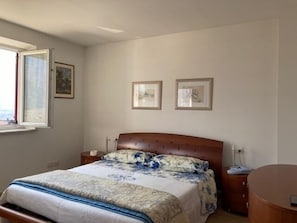 Ein Schlafzimmer mit einem Bett, einem Nachttisch, einem Beistelltisch, einem runden Holztisch und zwei gerahmten Bildern an der Wand.