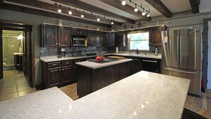 Une cuisine moderne avec des meubles en bois foncé, un grand îlot en granit, des appareils électroménagers en acier inoxydable et un pare-feu en pierre.