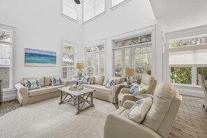 A spacious living room with a high ceiling, large windows, and a view of the outdoors.