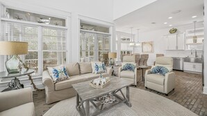En rummelig stue med en beige sofa, et sofabord og et spiseområde med stole.