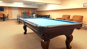 A pool table in a room with beige carpet, a television on the wall, and two patterned chairs. - 2-Bed. 2-Bath. Downtown Winter Park Condo CB2 (Winter Park)