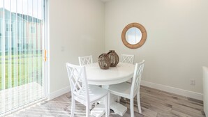 Un coin repas avec une table ronde, des chaises blanches et un miroir en bois accroché au mur.