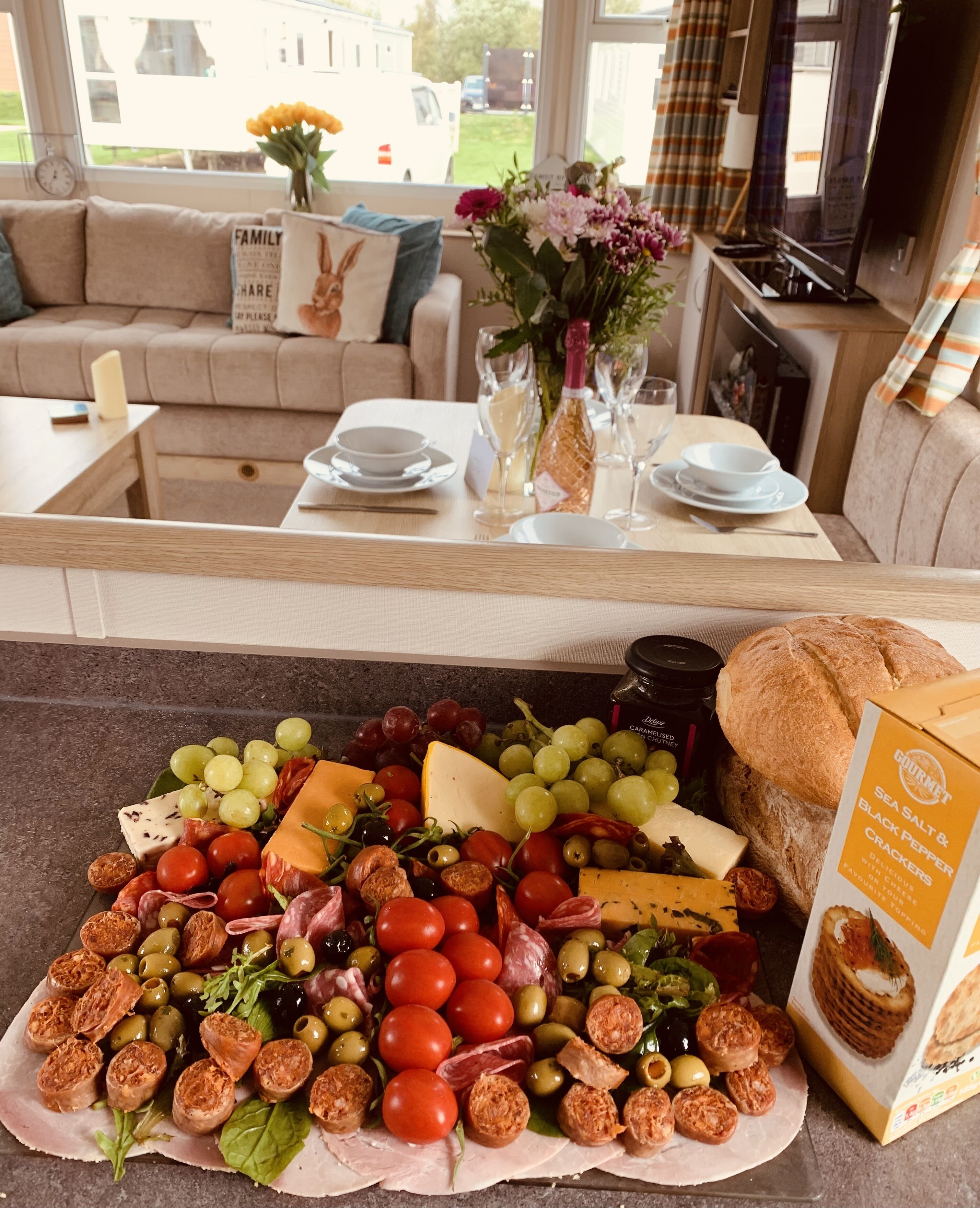 A dining area with a table set for two, featuring a variety of cheeses, meats, and olives.